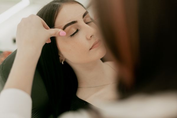 Beautician shaping a client's eyebrows in the studio