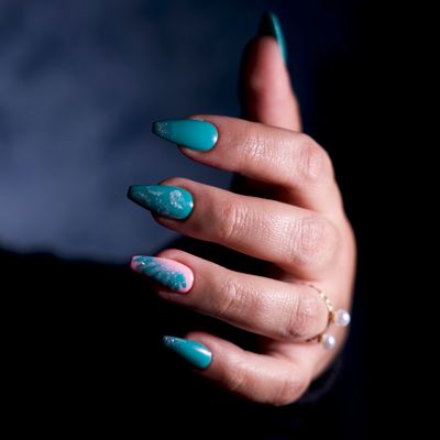 A hand with teal ombre glitter nail art against a dark background