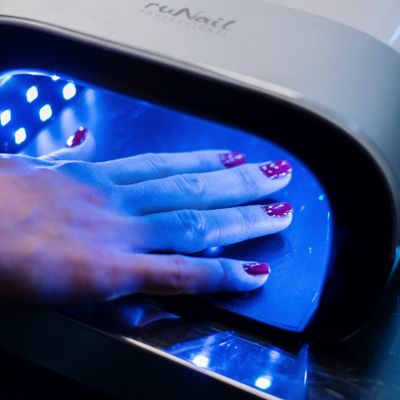 A hand with red-polished nails curing under a glowing UV lamp against a dark background
