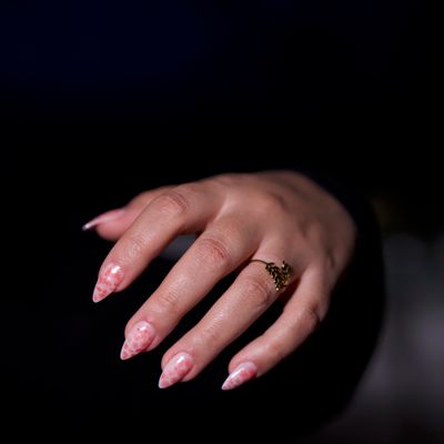 A hand with glossy pale pink stiletto nails against a black background