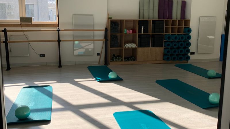 Open studio room with exercise mats, foam rollers and a barre, used for assessments and assisted stretching