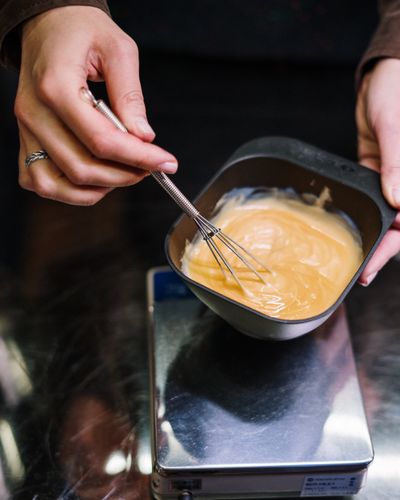 A stylist's hands whisking hair colour in a bowl set on a digital scale