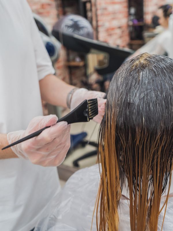 A colourist painting fresh colour through damp hair, root to end
