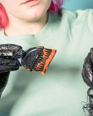 A colourist with a loaded vivid-orange tint brush, ready to apply
