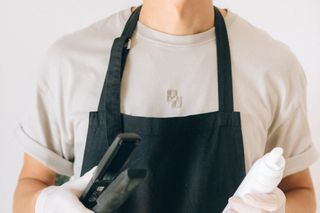 Tom Whitfield, a male hairdresser in a black apron, holding styling tools